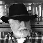 Author, Michael Simms. portrait in black-and-white. Michael is wearing a plaid shirt and a black hat.