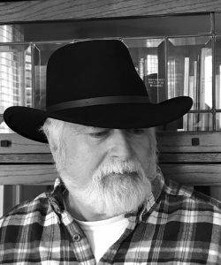 Author, Michael Simms. portrait in black-and-white. Michael is wearing a plaid shirt and a black hat.