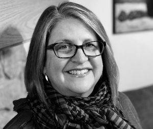 Poet, Lisa J. Parker. She has straight, shoulder-length hair, blond, with narrow rectangular glasses and a big toothy smile. The photo is in black and white. 