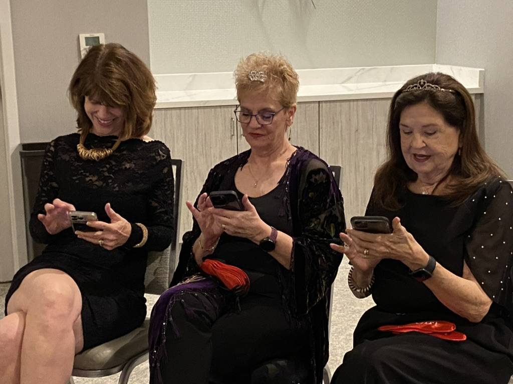 Three Pulpwood Queens atendees take a moment to check in with the outside world and scroll on their phone.