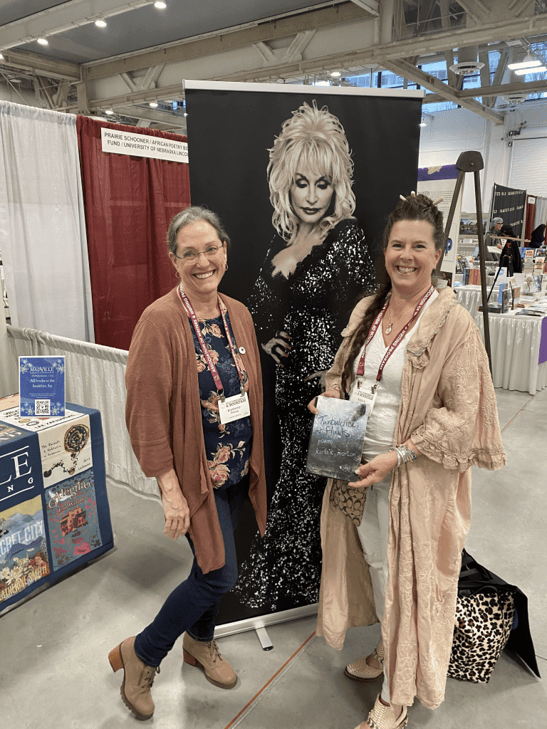 Former Texas Poet Laureate Karla K. Morton and Madville Publishing founder Kim Davis pose in front of the Dolly poster. Karla is holding a stack of copies of her poetry collection, Turbulence and Fluids.