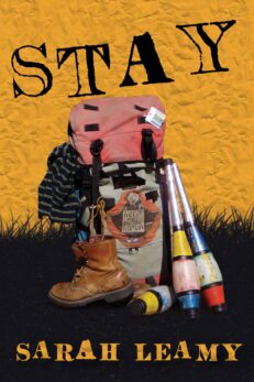 STAY, Sarah Leamy. These words appear on a background of mustard yellow sky over a black lawn. In the center of the field sits a worn rucksack with bits hanging out, a boot, juggling clubs, a striped sweater. A patch on the rucksack says "help me to be human"