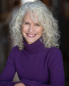 Author BettyJoyce Nash has curly, shoulder-length gray hair and a broad smile. She wears a plum-colored turtle-neck sweater.