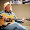 Author, musician Michael Amos Cody wearing a straw hat and strumming a guitar.