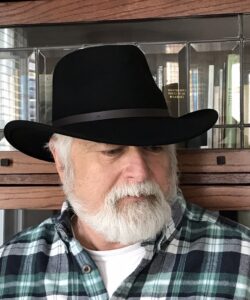 Author Michael Simms. Michael is a White man with a white beard and a black hat. In this photo he wears a checked shirt.