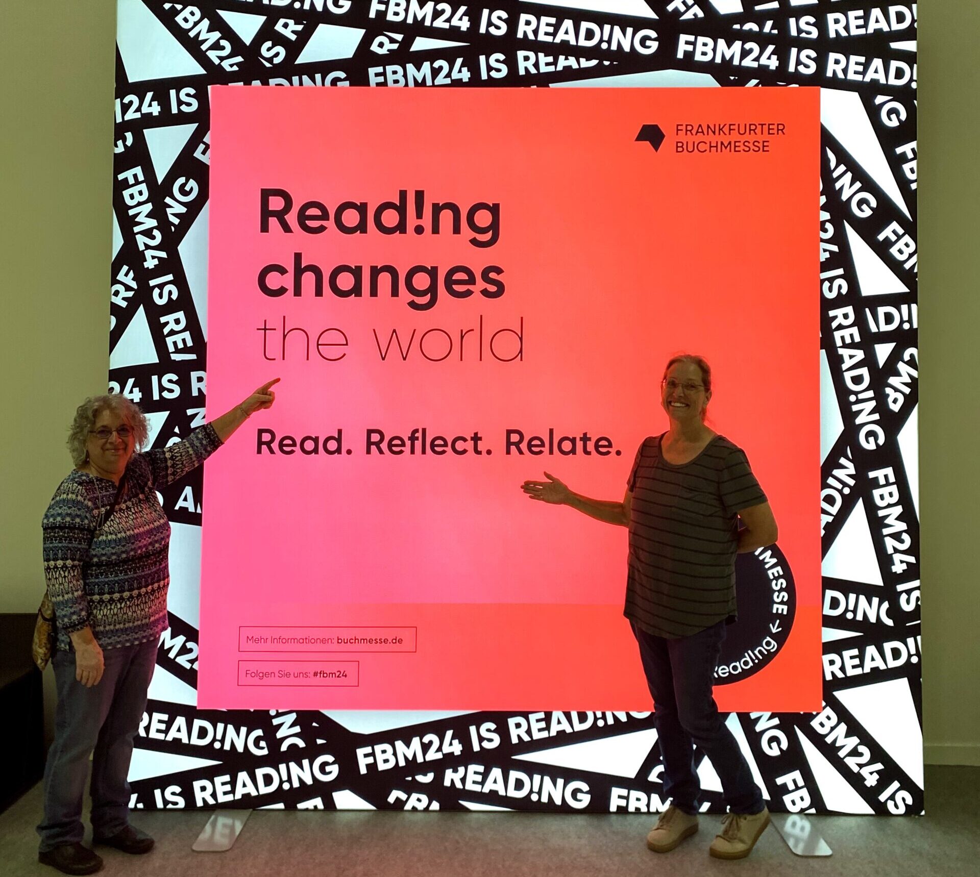 Kasey Rogers and Kim Davis pointing at one of the many bright pink signs at the Frankfurter Buchmesse. This one says "Reading Changes the World"