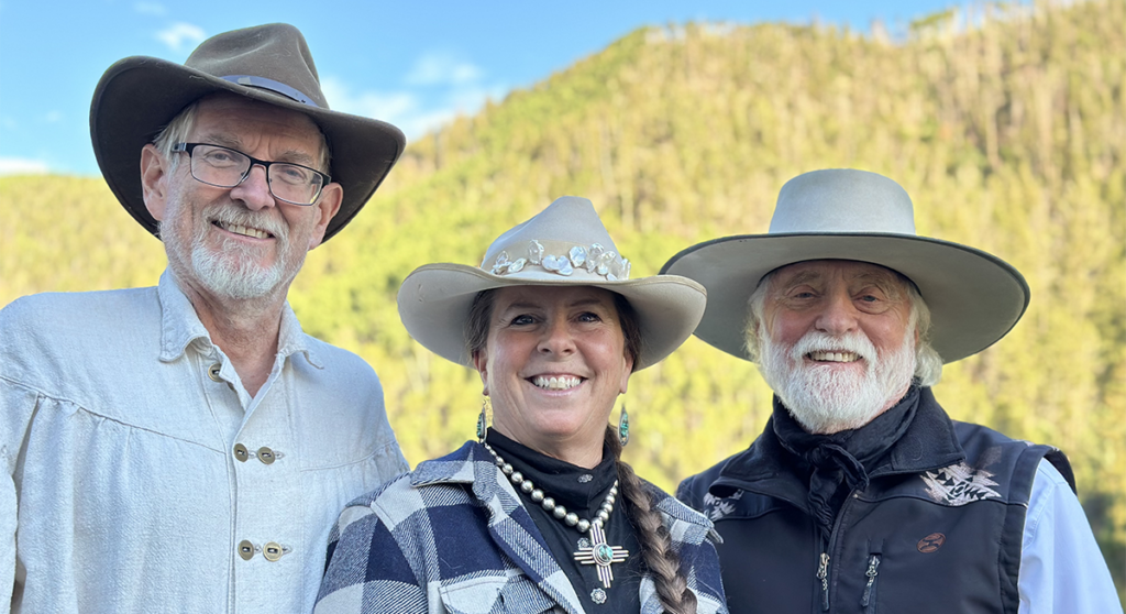 Texas poets laureate Alan Birkelbach and karla k. morton with musician, Michael Martin Murphey. All wear cowboy hats and big smiles. Behind them is a hillside covered in trees with yellow folliage.