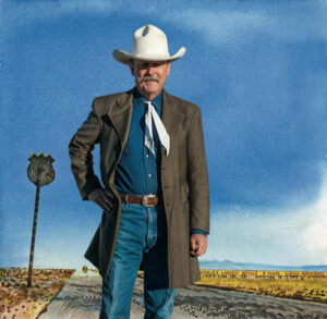 Artist Bob Boze Bell standing on historic Route 66. Bob wears a white cowboy hat, long cowboy coat and jeans, and the blue sky behind him goes on and on.