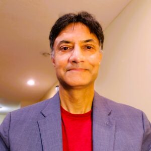 Author Dr. Goutham Rao. He is a tan skinned man with short dark hair, a red t-shirt, a gray suitcoat, and an enticing smile on closed lips.