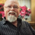 Author Michael Amos Cody is a smiling man with glasses and a beard and a bald head.