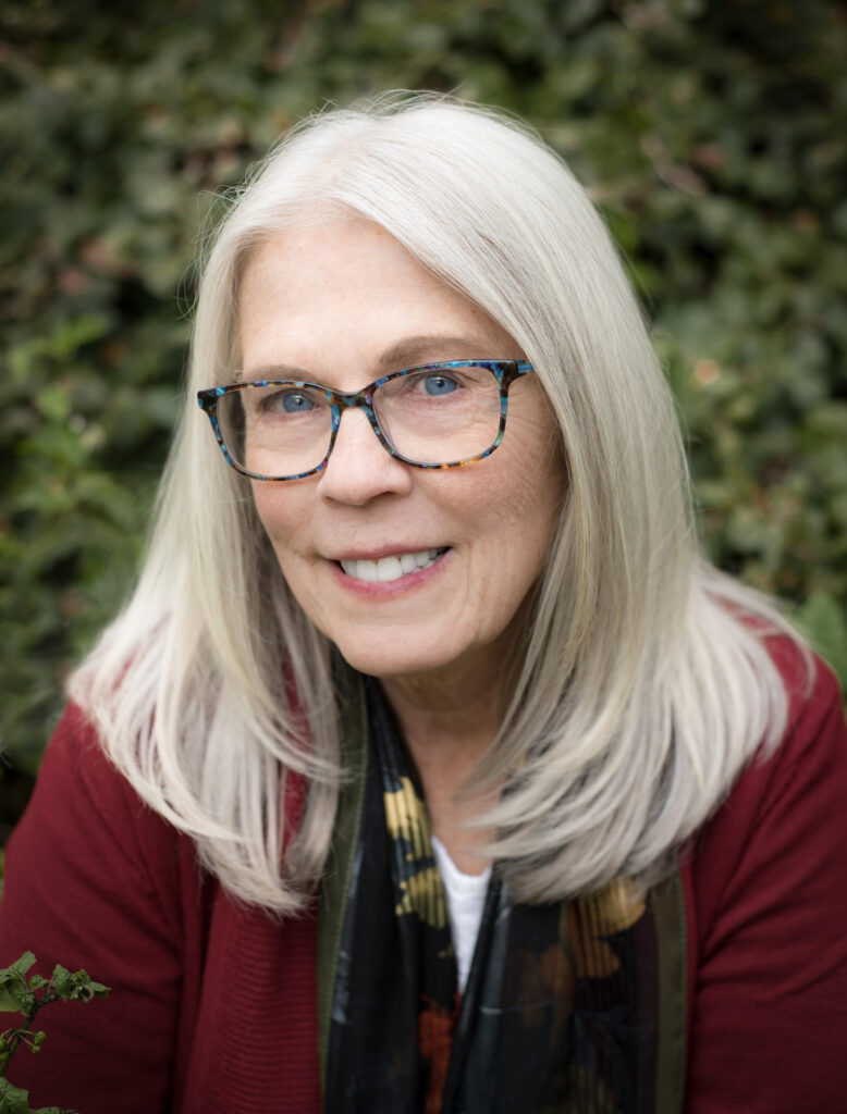 Poet Kari Gunter-Seymour is a white-haired woman with glasses and a lovely warm smile. She's wearing a burgundy-colored sweater.