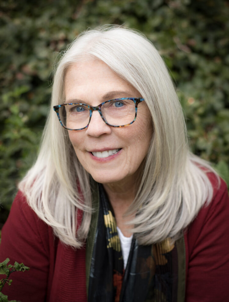Poet Kari Gunter-Seymour is a white-haired woman with glasses and a lovely warm smile. She's wearing a burgundy-colored sweater.