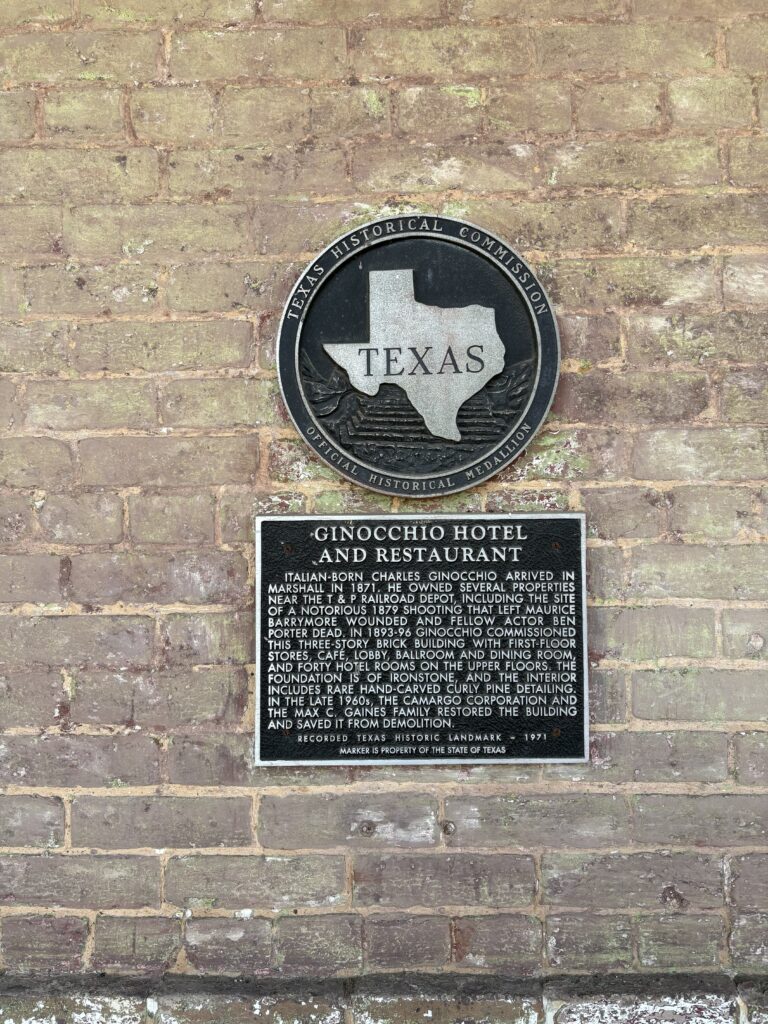 Official Texas Historical Marker outside the entrance to Ginocchio. It says: "Ginocchio Hotel and Restaurant. Italian-born Charles Ginocchio arrived in Marshall in 1871. He owned several properties near the T & P Railroad Deopt, including the site of a notorious 1879 shooting that left Maurice Porter dead. In 1893-96, Ginocchio commissioned this three-story brick building with first-floor stores, card, lobby, ballroom and dining room, and forty hotel rooms on the upper floors. The foundation is of ironstone, and the interior includes rare hand-carved curly pine detailing In the late 1960s, the camargo corporation and the Max C. Gaines family restored the building and saved it from demolition. RECORDED TEXAS HISTORIC LANDMARK - 1971