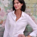 Author Kerry Neville. She wears a simple white blouse, has shoulder length dark hair and enormous eyes. 
